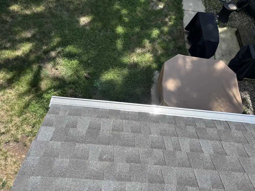 Continuous perforated gutter guard beside gray shingles in Gibbsboro